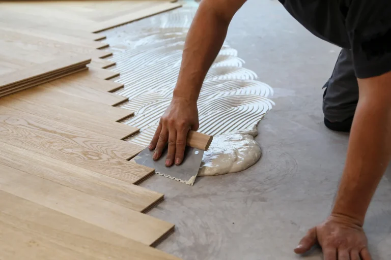 A person installing wooden flooring with adhesive on the subfloor